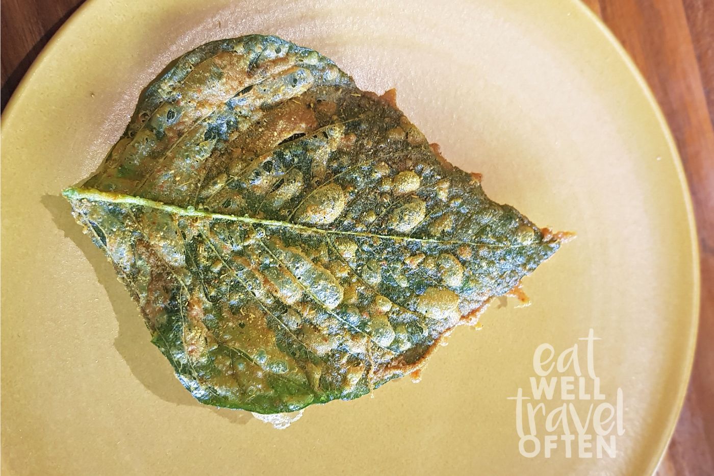 A green leaf on a yellow plate that is blistered with a coating of spices