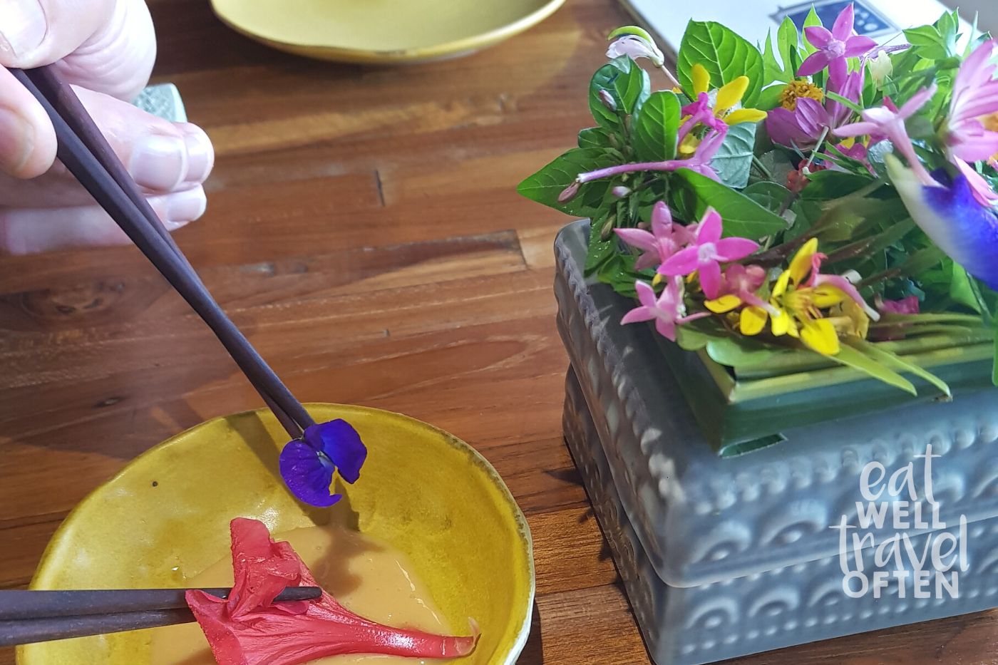 Chopsticks picking up bright coloured flowers in a yellow bowl